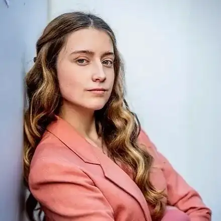 Portrait of Isabel Martin-Horvath in a coral blazer, leaning against a pale wall.